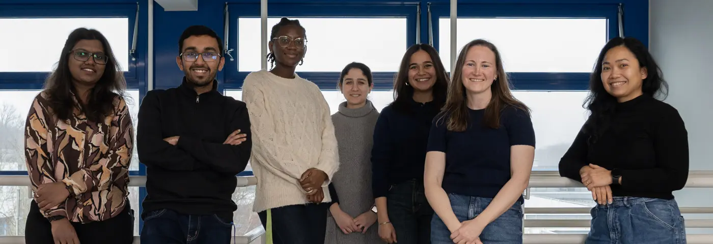Group photo of the Materials-Host Interactions team indoors at INM; the team members are standing together in front of large windows.